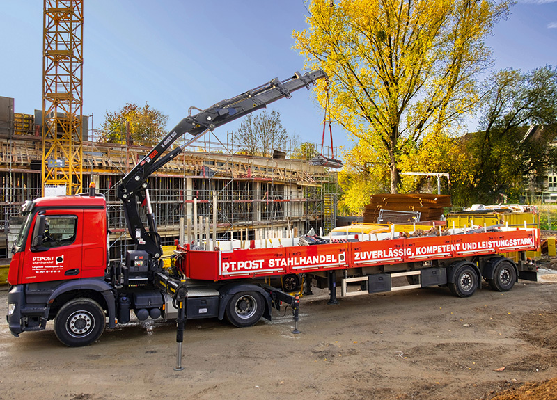 Ein grosser Lkw entlädt mit einem Kran Baueisen auf einer Baustelle